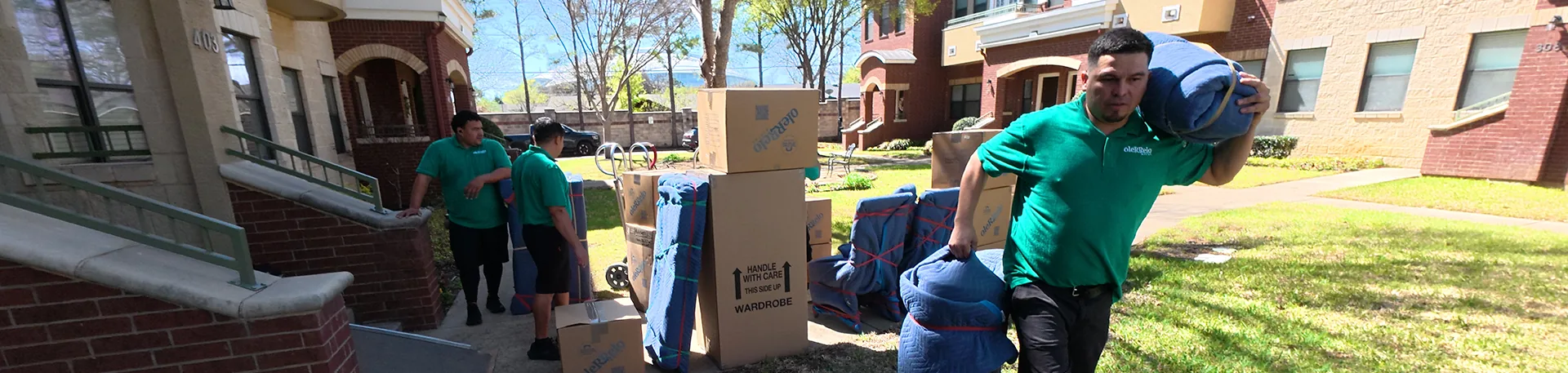 Oler Relo Moving Crew Loading an In-State Move Oler Relo Moving crew carrying blanket-wrapped furniture and boxes outside a home during an in-state move